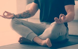 Imagem de homem jovem meditando na sal de casa. Meditação - Benefícios e como começar - Dra Ana Luiza Cardoso - Endocrinologista