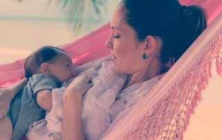 Dra. Ana Luiza Cardoso amamentado sua filha em uma rede, na praia. Aleitamento materno e amamentação